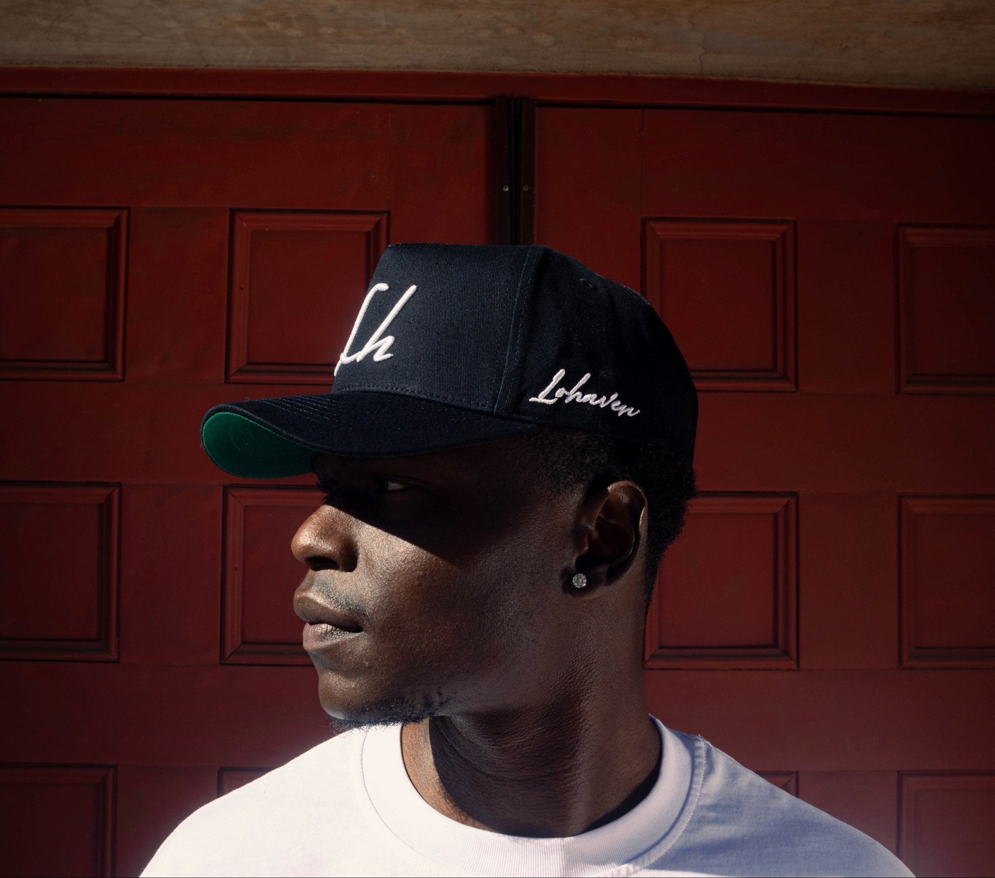 Person wearing a black cap with white text against a red door background